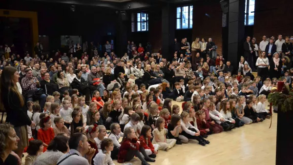 Rodzice i dzieci zgromadzeni w auli szkolnej w czasie świątecznego spotkania dla klas wczesnoszkolnych.