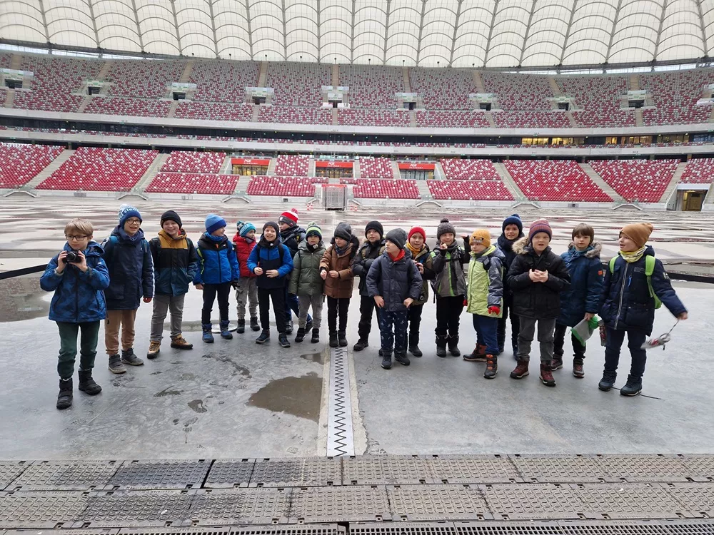 Uczniowie klasy 2D na płycie Stadionu Narodowego pozujący do zdjęcia.