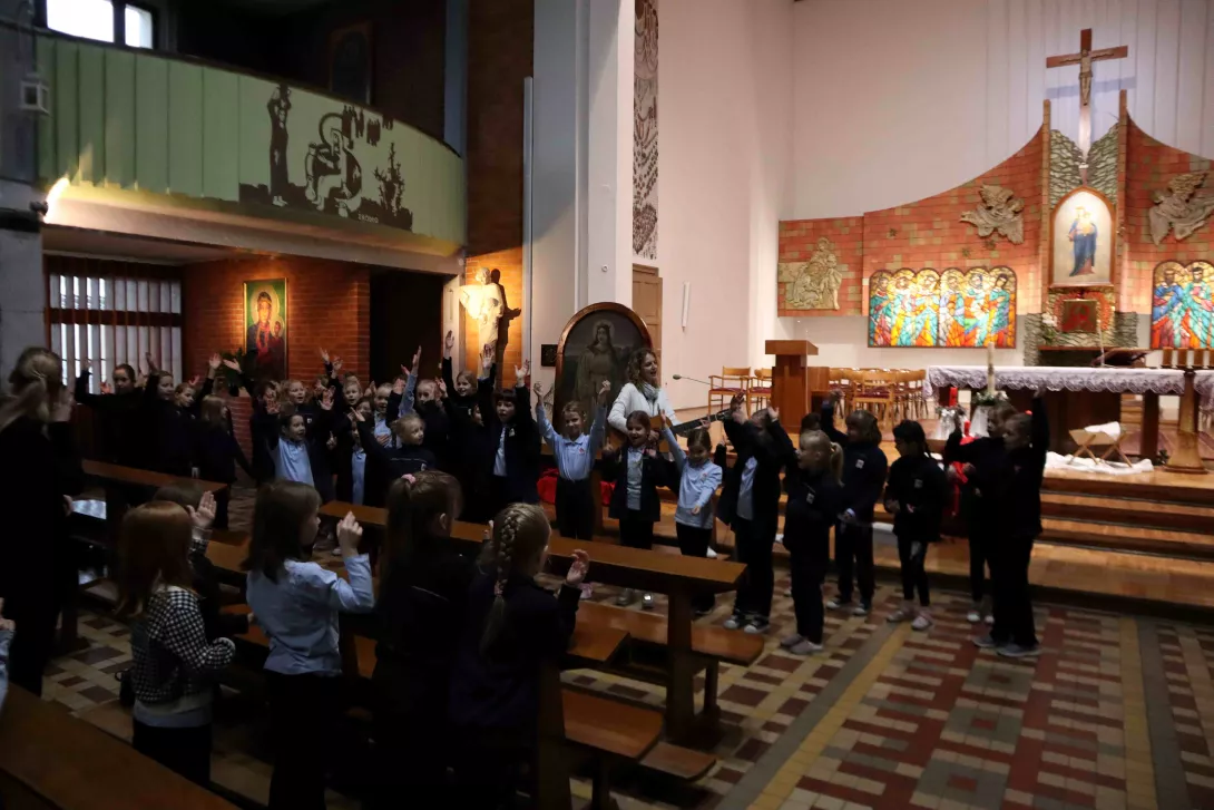 Śpiewająca schola klas 1-3, z grającą na gitarze panią Anetą Bartłomiejczyk-Siuto.
