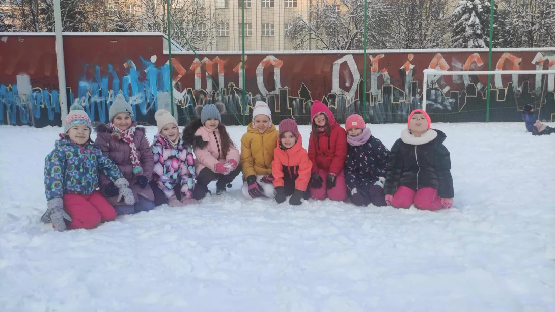 Uczennice klasy 1a siedzące w śniegu podczas porannej gimnastyki na boisku szkolnym