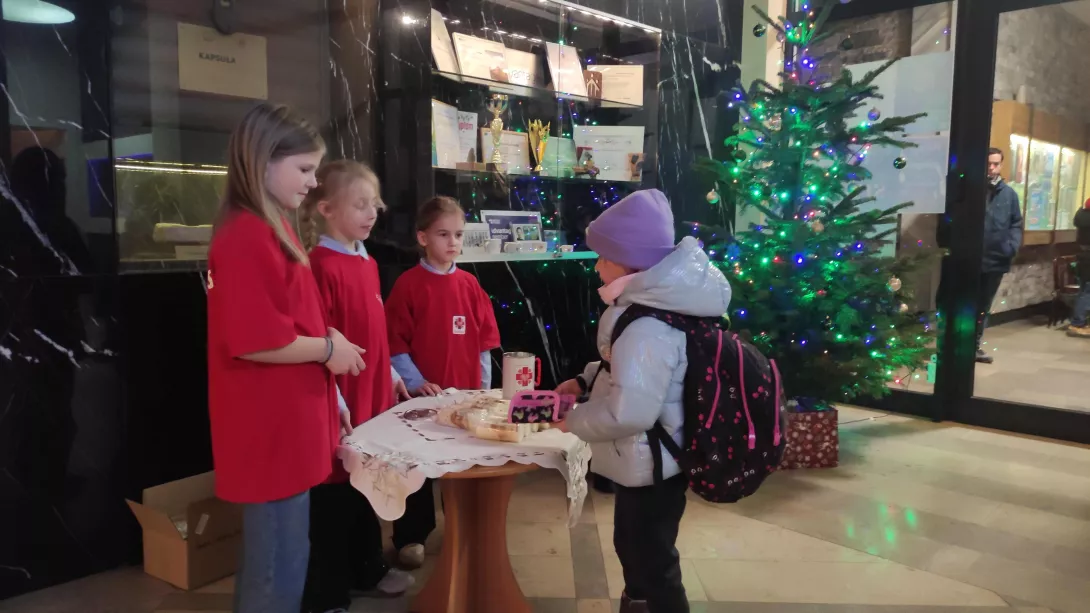 Wolontariuszki SKC sprzedające świece w szkolnym holu w ramach akcji Wigilijne Dzieło Pomocy Dzieciom Caritas Polska w dniach 14-16 grudnia 2025