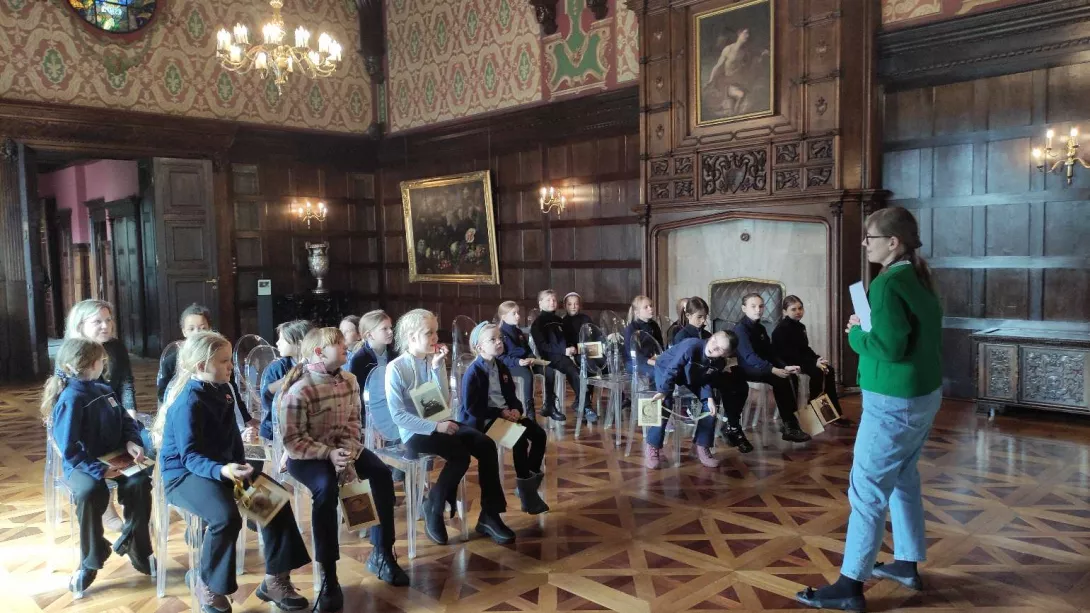 Uczennice w sali balowej podczas quizu pytań prowadzonym przez panią przewodnik 