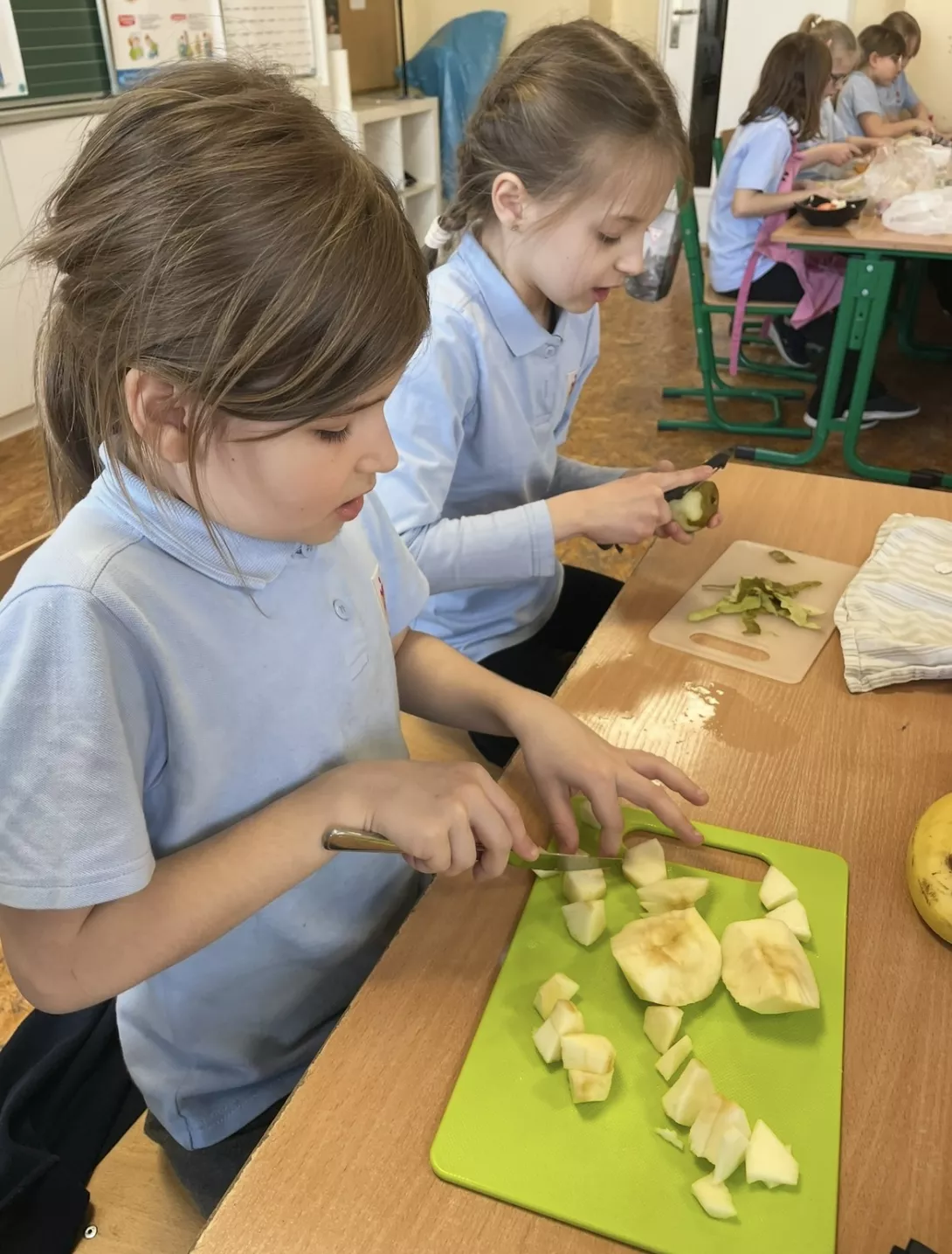 Uczennice przygotowują sałatkę owocową.